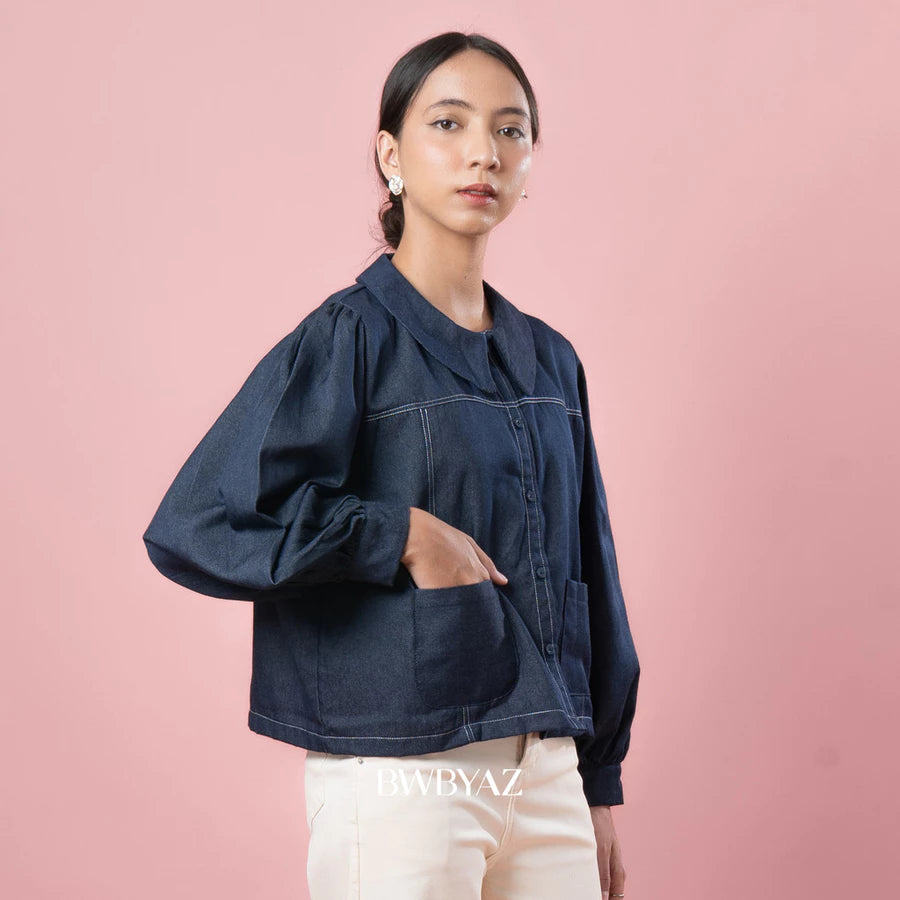 Woman wearing a indigo blue denim jacket against a pink background with 'BWBYAZ' branding.