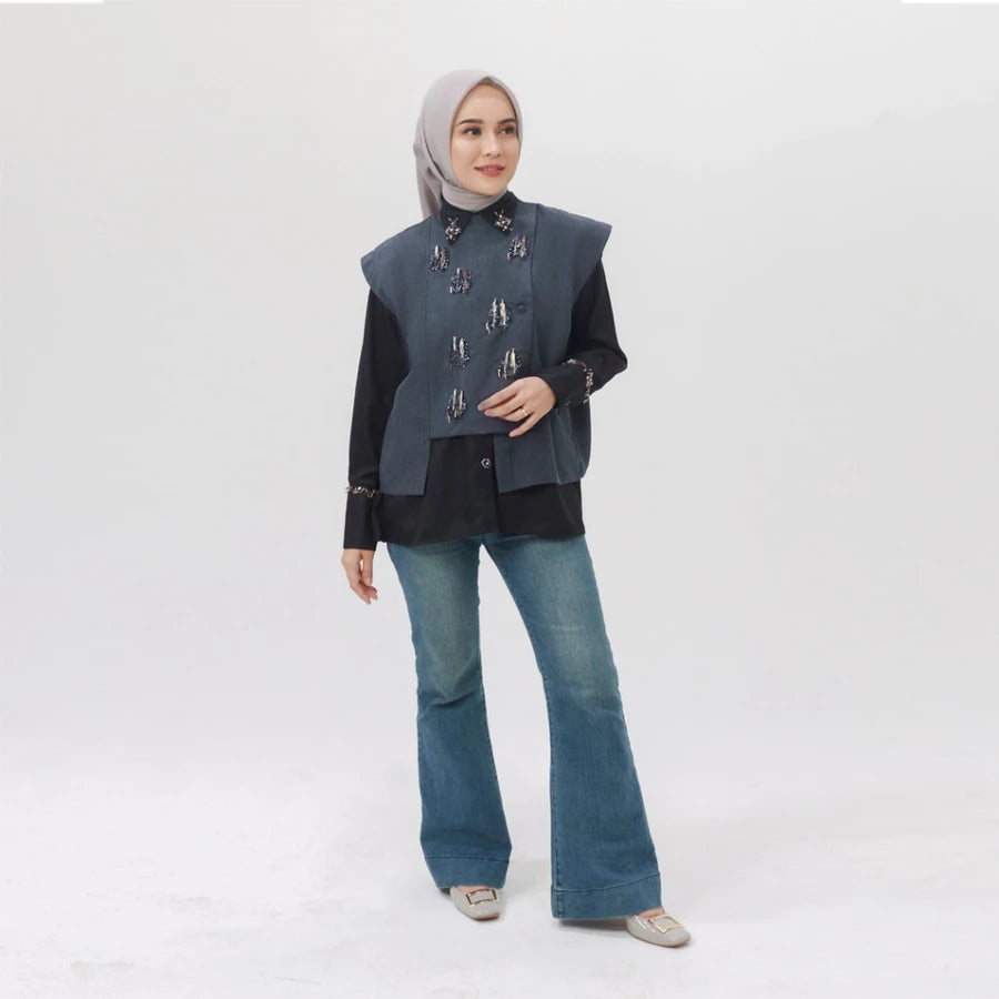 Woman wearing a dark grey vest over a black top and blue jeans on a white background