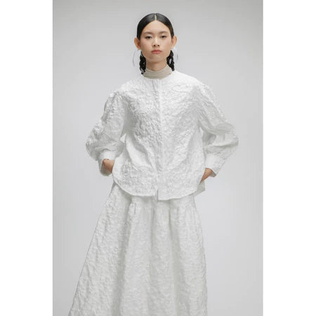 Person wearing a white textured puffy shirt on a plain background