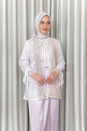 Woman wearing a white lace outer by Kartinis Label and hijab against a white curtain background