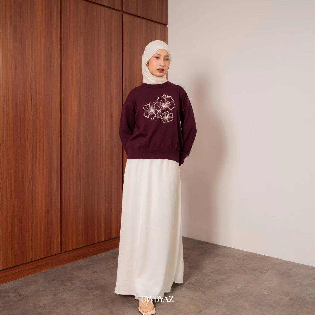 A person wearing a wine-colored sweater with a floral embroidery design on the front from BWBYAZ, paired with a white skirt and a white headscarf.