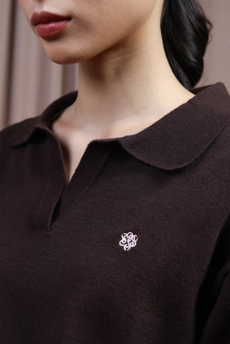 Close-up of a person wearing a dark brown knit polo knit top by Hijabchic with a small white embroidered logo on the chest.