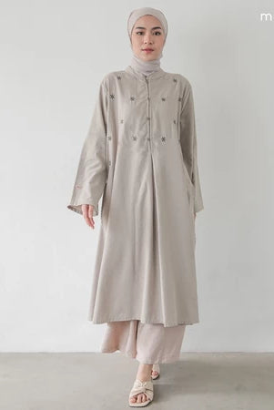 Seorang wanita memakai Fara Tunik, tunik berlengan panjang dengan material soft flanel dan memiliki aksen bunga, berwarna taupe.
