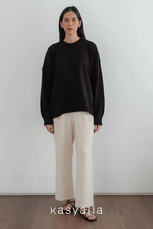 Woman wearing a black oversized sweater and beige pants against a white wall with 'kasyalia' branding.