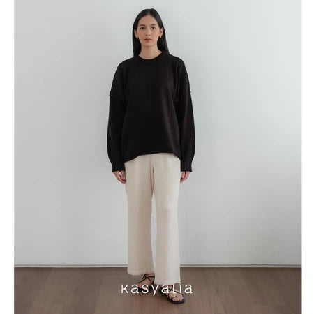 Woman wearing a black oversized sweater and beige pants against a white wall with 'kasyalia' branding.