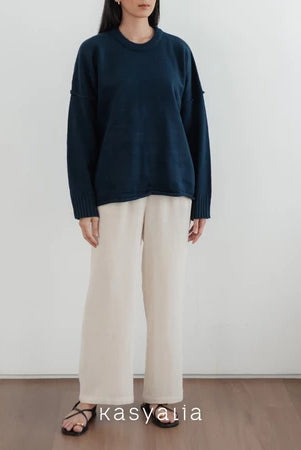 Person wearing a navy oversized sweater and beige pants against a white wall with 'kasyalia' branding.