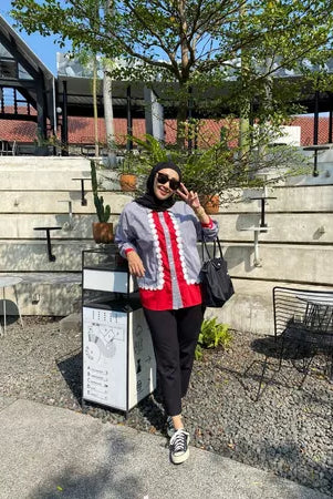 A woman wearing a casual modest shirt by Abame featuring a red base color with gray panels and white ruffle details down the front.