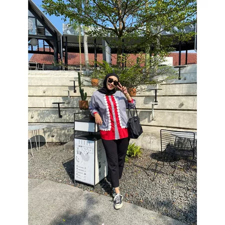 A woman wearing a casual modest shirt by Abame featuring a red base color with gray panels and white ruffle details down the front.