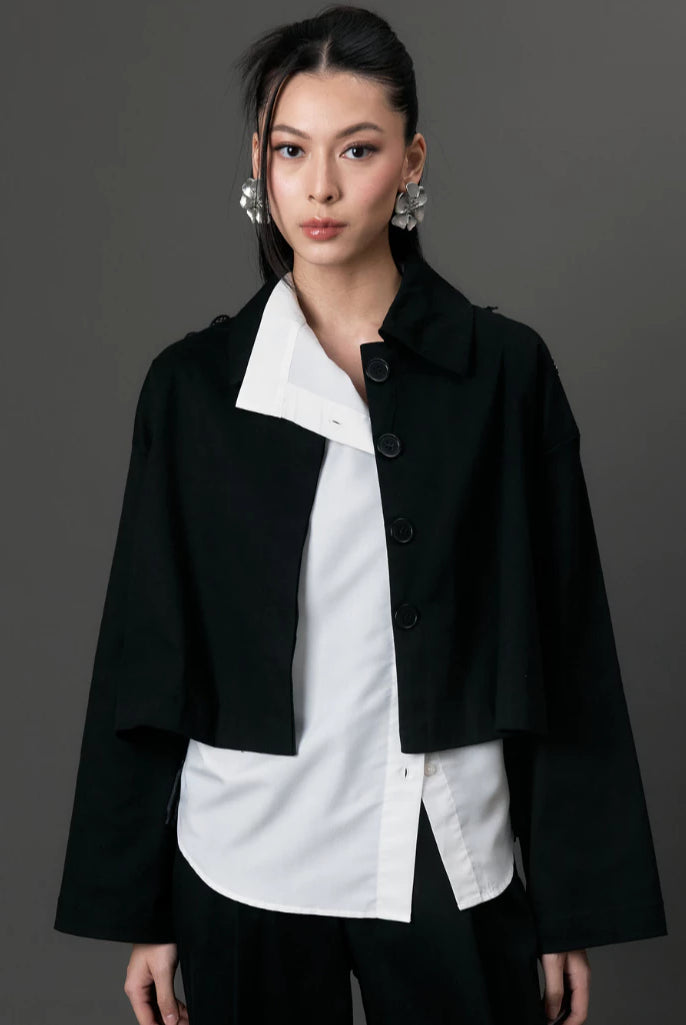 Woman wearing a black coat by Studio Tui over a white shirt on a gray background