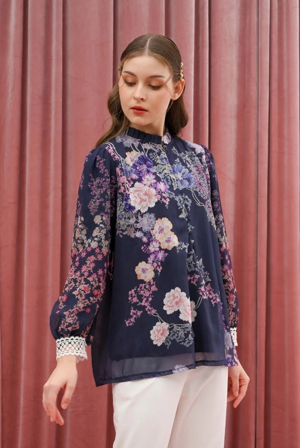 Woman wearing a floral navy blouse by Kasa Heritage against a pink curtain background