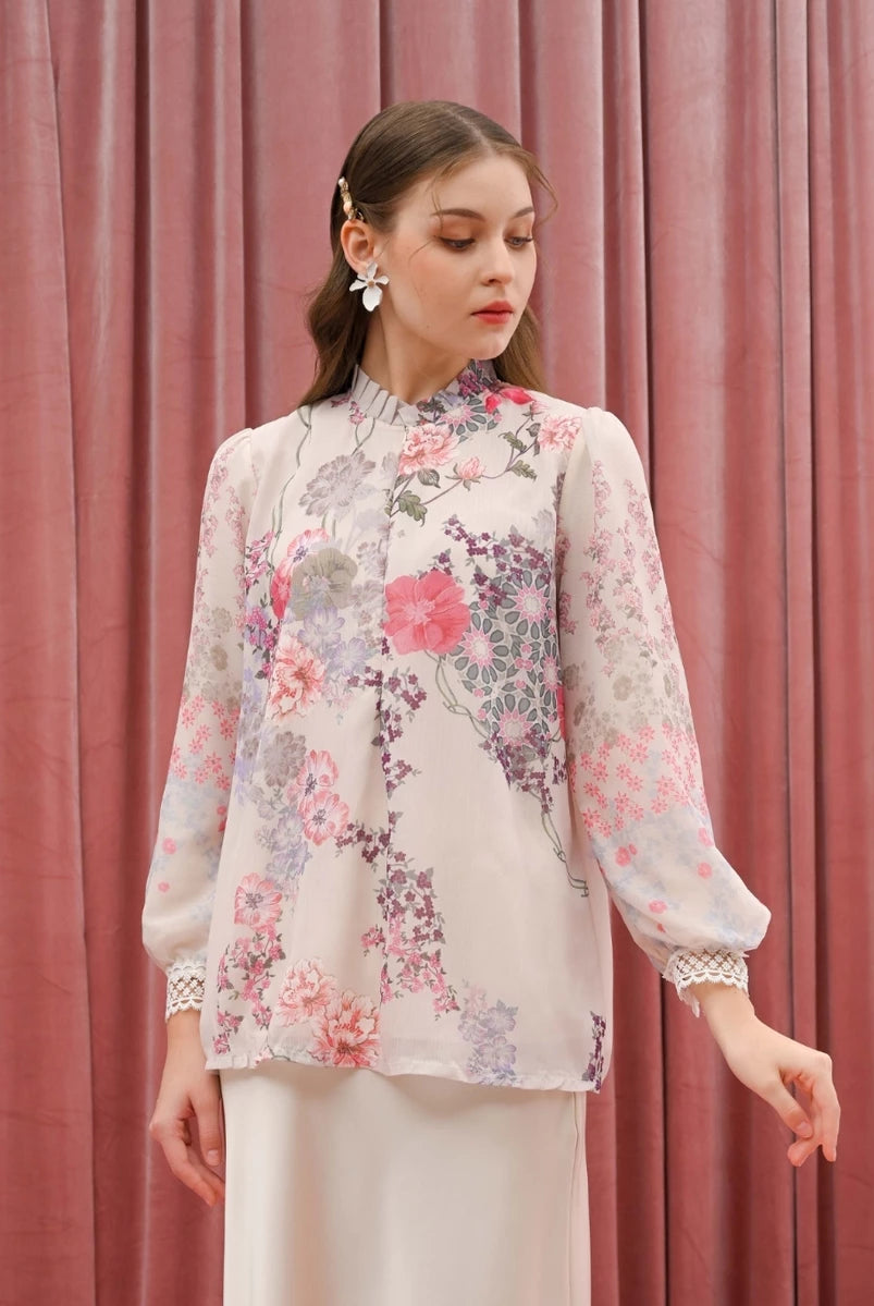 Woman wearing a floral beige blouse by Kasa Heritage against a pink curtain background