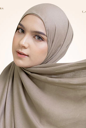A woman wearing a beige pashmina viscose draped around her head, with the brand 'Puru Kambera' visible on the scarf.