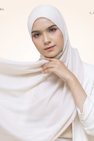 A woman wearing a broken white pashmina viscose draped around her head, with the brand 'Puru Kambera' visible on the scarf.