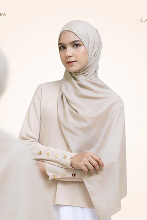 A woman wearing a light beige pashmina viscose draped around her head, with the brand 'Puru Kambera' visible on the scarf.