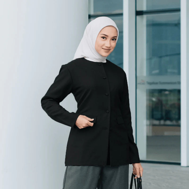 Woman wearing a black blazer from Atala Scarves and hijab standing in front of a glass door.