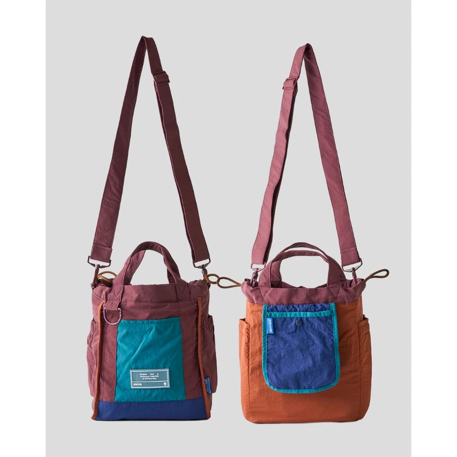 Women’s reversible tote bag by Muhajir Project featuring two looks in one design. One side comes in burgundy with navy blue accents and a teal front pocket, while the other side shows a brown body with a contrasting navy blue pocket. Designed with adjustable shoulder straps, top handles, and side drawstring details for a practical and versatile everyday bag.