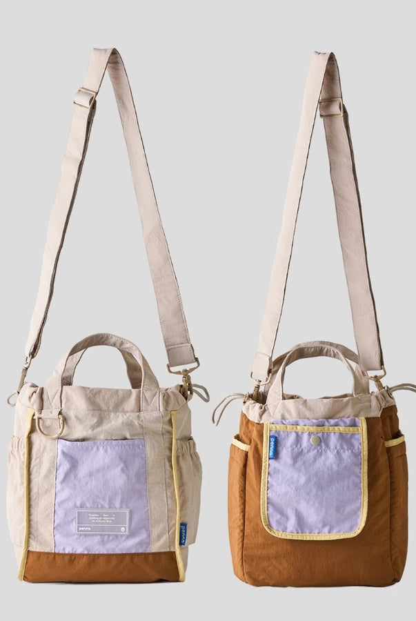 Women’s reversible tote bag by Muhajir Project featuring two looks in one design. One side comes in beige with brown accents and a lilac front pocket, while the other side shows a brown body with a contrasting lilac pocket. Designed with adjustable shoulder straps, top handles, and side drawstring details for a practical and versatile everyday bag.