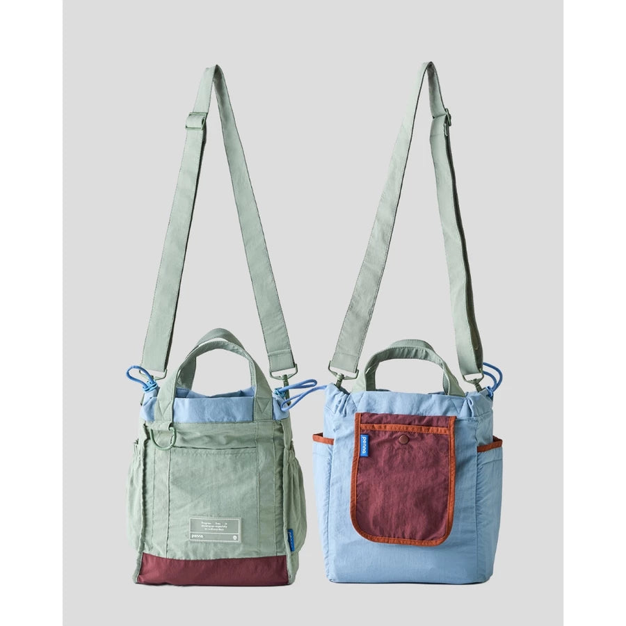 Women’s reversible tote bag by Muhajir Project featuring two looks in one design. One side comes in sage green with maroon accents and a clean front pocket, while the other side shows a light blue body with a contrasting maroon pocket. Designed with adjustable shoulder straps, top handles, and side drawstring details for a practical and versatile everyday bag.