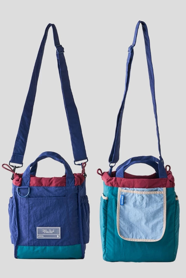Women’s reversible tote bag by Muhajir Project featuring two looks in one design. One side comes in navy blue with teal accents and a clean front pocket, while the other side shows a teal body with a contrasting light blue pocket. Designed with adjustable shoulder straps, top handles, and side drawstring details for a practical and versatile everyday bag.