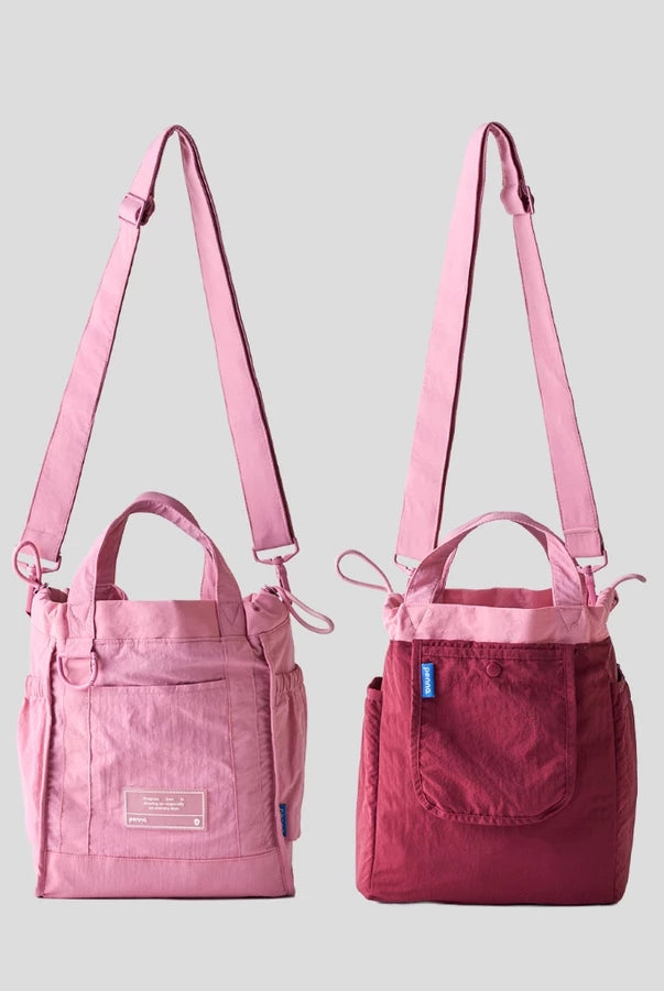 Women’s reversible tote bag by Muhajir Project featuring two looks in one design. One side comes in pink and a clean front pocket, while the other side shows a maroon with pink accents. Designed with adjustable shoulder straps, top handles, and side drawstring details for a practical and versatile everyday bag.