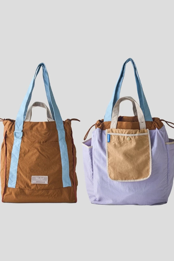 Reversible tote bag by Muhajir Project displayed in two sides, showing dual-color design with light blue and brown combination on one side and lilac with light brown pocket on the other. This versatile women’s bag features long shoulder straps, side drawstring details, and a functional front pocket, highlighting its practical and stylish two-in-one design.