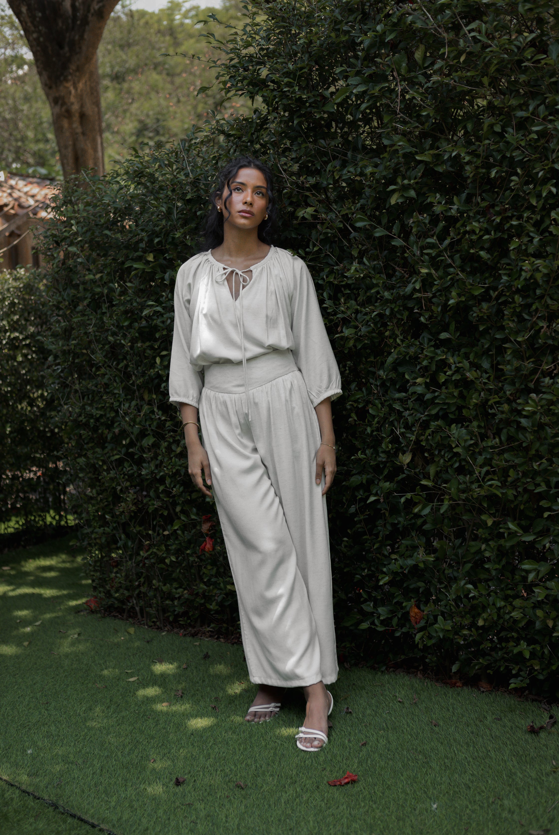 Woman in a white top and linen pants by Kasyalia standing in a garden setting