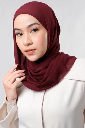Woman wearing a maroon pashmina hijab by Tantri Namirah Official against a light gray background