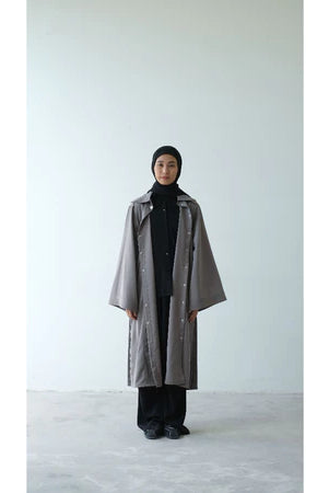 Person wearing a long gray coat from Rashawl and black hijab on a white background