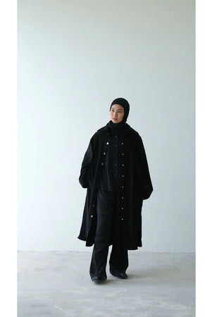 Person wearing a long black coat by Rashawl and black pants on a white background