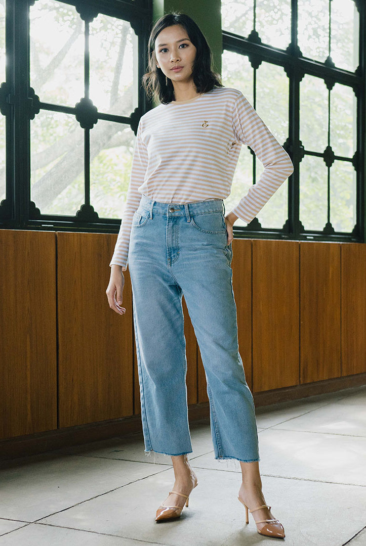 A woman standing in an indoor location with wooden paneling in the background, wearing light blue denim pants and a striped long-sleeve top.
Seorang wanita berdiri di dalam ruangan dengan panel kayu sebagai latar belakangnya, mengenakan celana denim biru muda dan atasan lengan panjang bergaris.