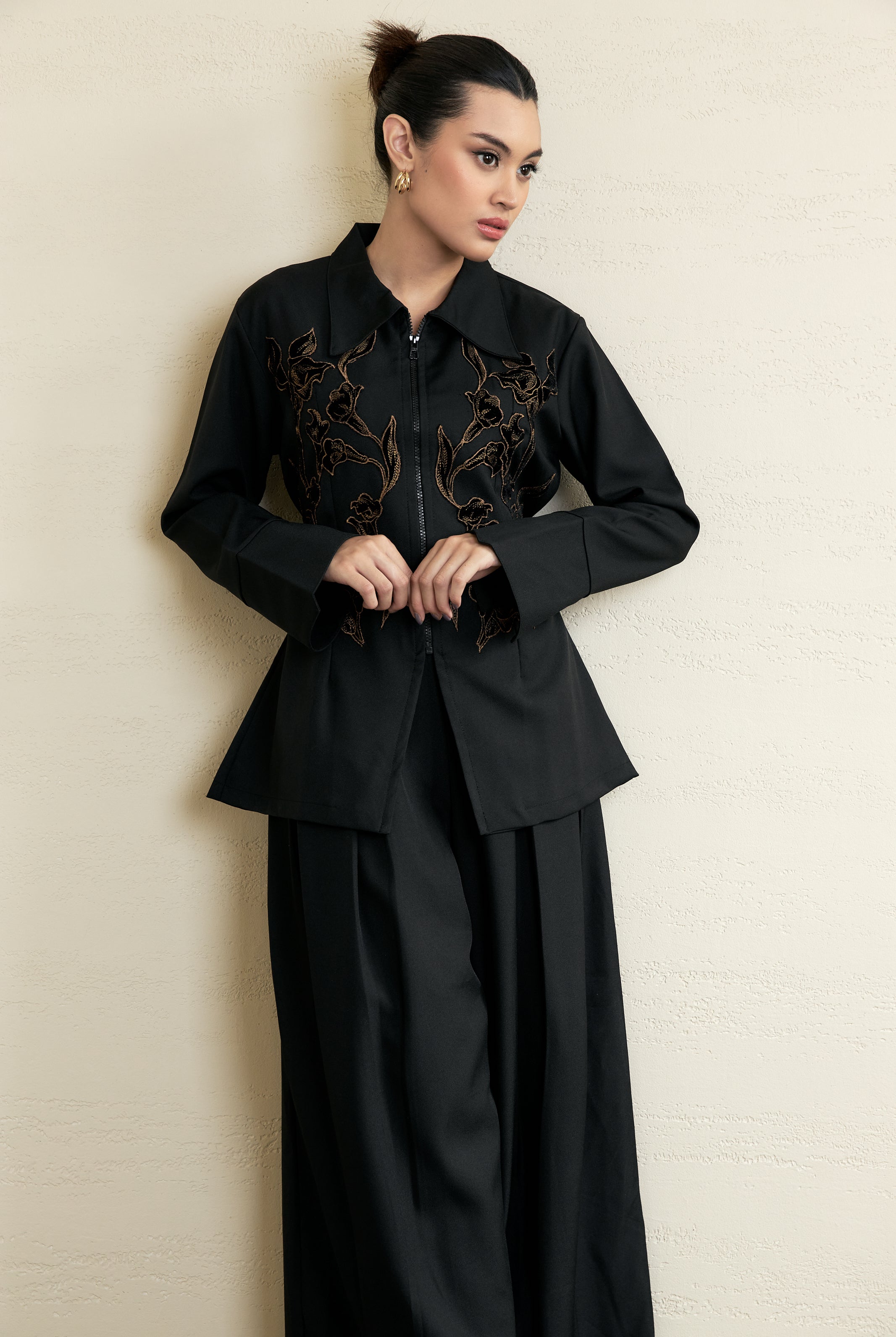 Woman wearing a black outfit with intricate designs by Studio Tui against a beige background