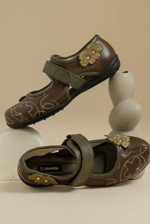 Pair of dark brown flat shoes with floral designs by Dianable on a beige background