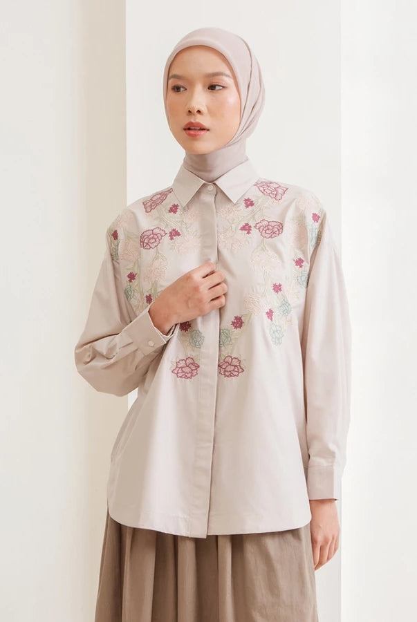Woman wearing a beige shirt with floral embroidery by Hijabchic against a white background