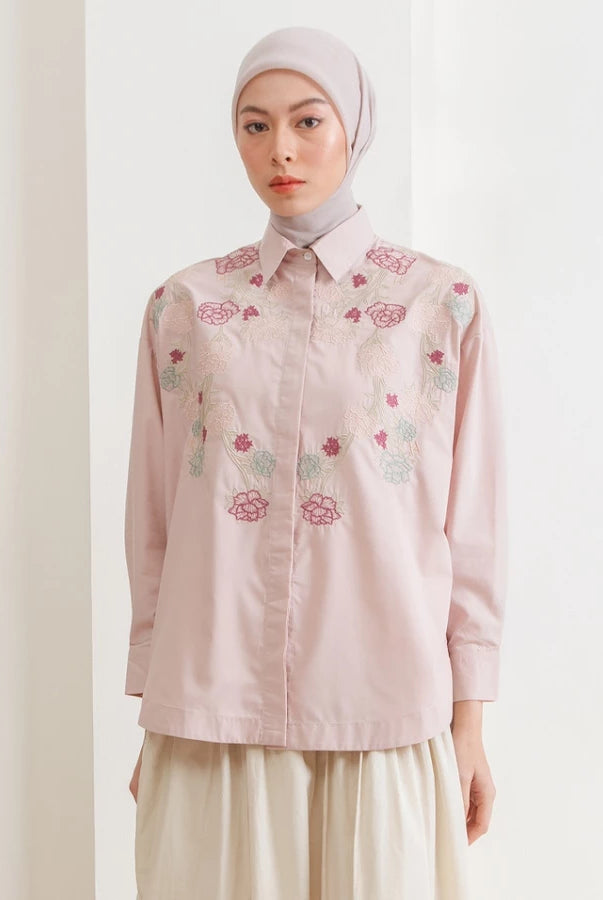 Woman wearing a light pink shirt with floral embroidery by Hijabchic on a plain background