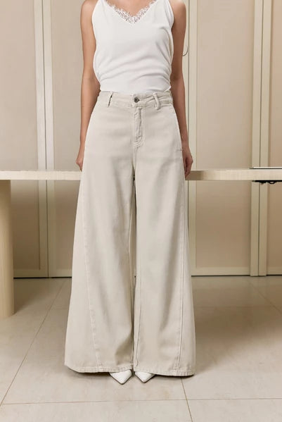 Person wearing a white sleeveless top and white wide-leg jeans pants by Studio Tui in a minimalistic setting.