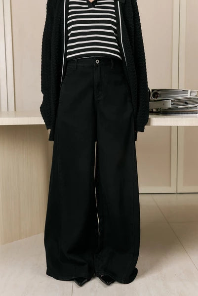 Person wearing a black cardigan, striped shirt, and wide-leg jeans pants by Studio Tui in an indoor setting.