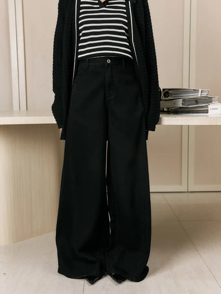 Person wearing a black cardigan, striped shirt, and wide-leg jeans pants by Studio Tui in an indoor setting.