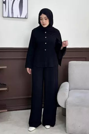 Person wearing a black outfit by Renaette in a room with a clock and chair.