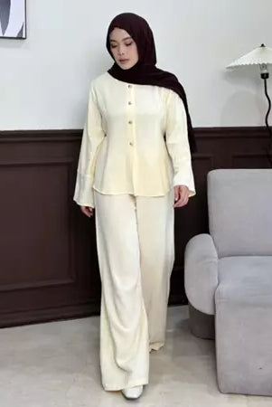 Woman in a cream outfit by Renaette standing in a room with a gray chair and white wall.