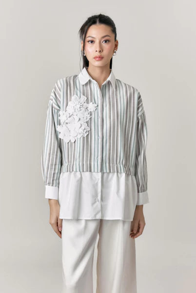 Woman wearing a striped shirt with floral details and white pants by Studio Tui on a plain background