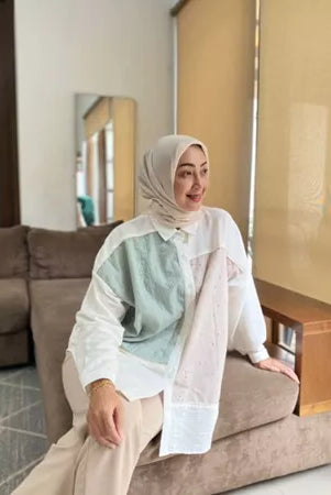 Person wearing a white shirt with green and beige accents by Abame and beige hijab indoors.