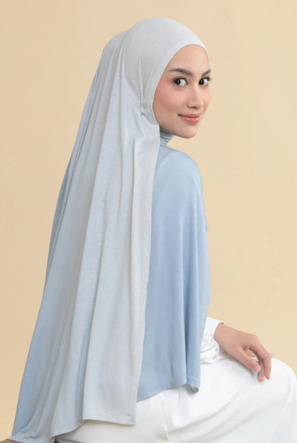 Woman wearing a light blue hijab shawl by Lozy Hijab and white outfit on a beige background