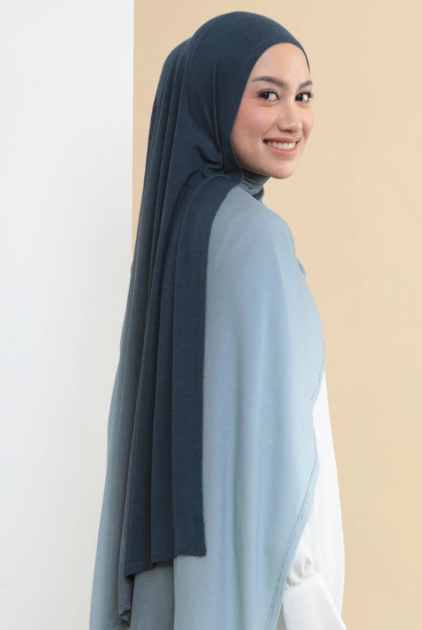 Woman wearing a dark blue hijab shawl by Lozy Hijab and light blue top on a beige background