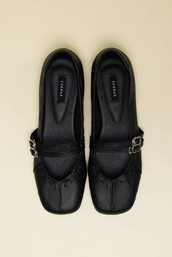 A pair of black pebbled leather Mary Jane flatshoes with silver-tone buckle straps by Cekhas, shown from a top-down view on a light beige background.