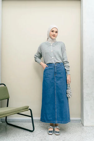 Woman wearing a gray shirt and blue denim skirt from Haidee Orlin standing in a room with a chair.