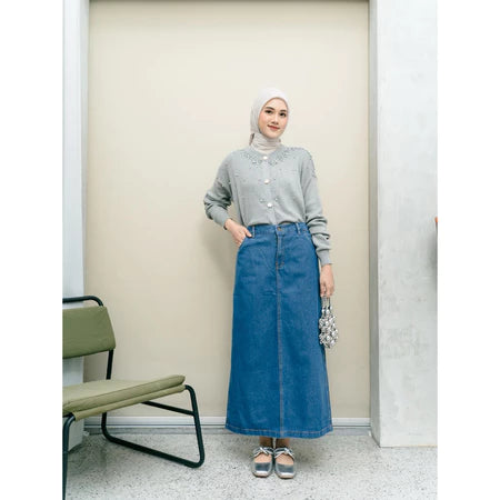 Woman wearing a gray shirt and blue denim skirt from Haidee Orlin standing in a room with a chair.