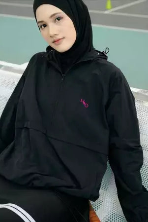 Person wearing a black windbreakers by Haidee Orlin with a logo on a sports court