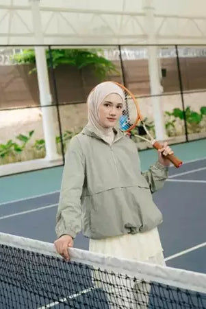 Person wearing a sage green windbreakers by Haidee Orlin with a logo on a sports court