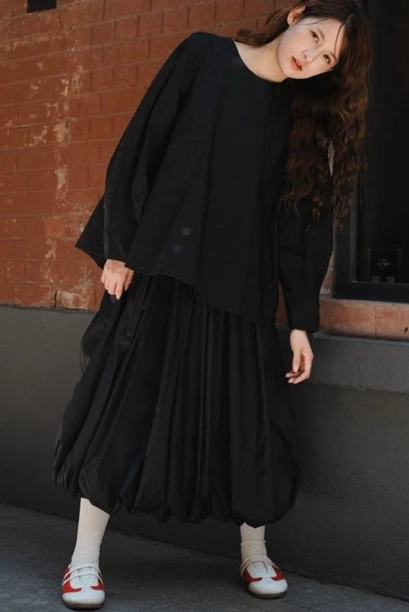 Person wearing a black blouse by Yestoday with white shoes against a brick wall.