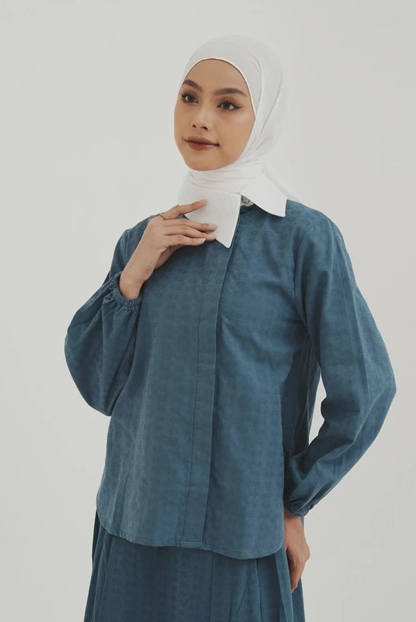 Woman wearing a blue denim shirt by Tunique with a white hijab on a plain background